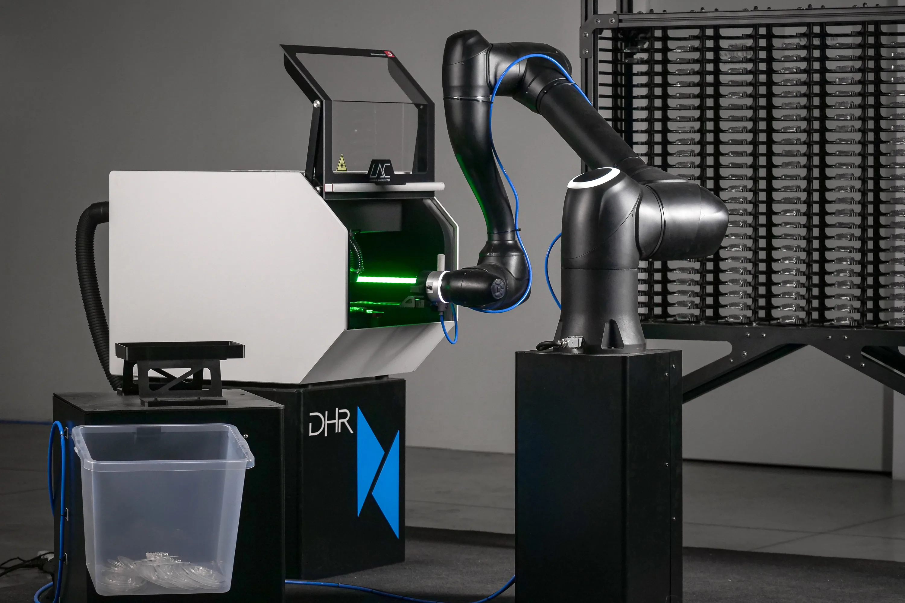 The image features a DMU LAC laser aligner cutter in a custom robotic cell, with a cobot arm, multiple storage racks, and sorting trays, illustrating advanced clear aligner cutting automation for fully autonomous dental manufacturing. 