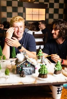 Two people sitting on a table with figurines in front of them