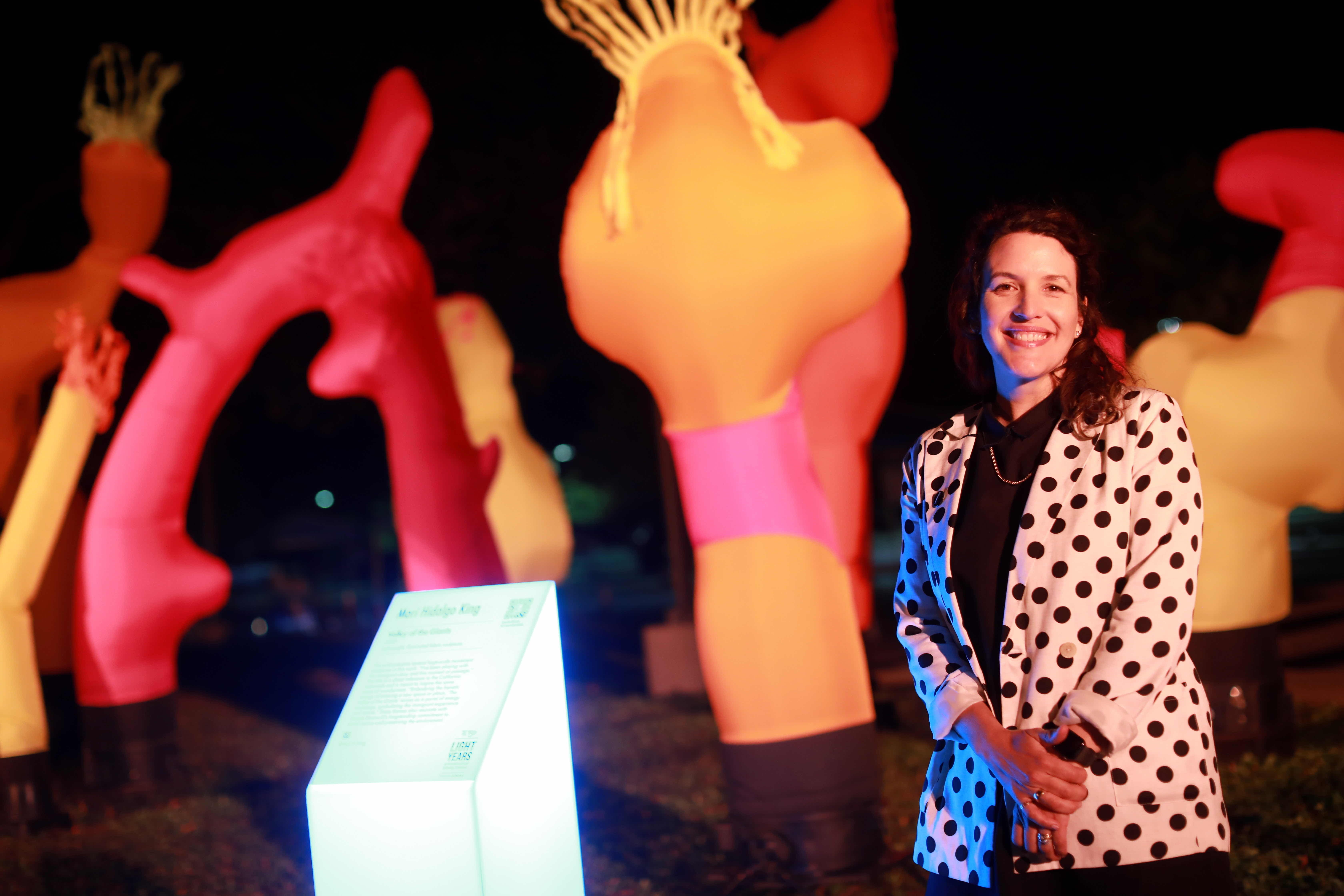 A person stands beside colorful, illuminated sculptures in a nighttime setting.