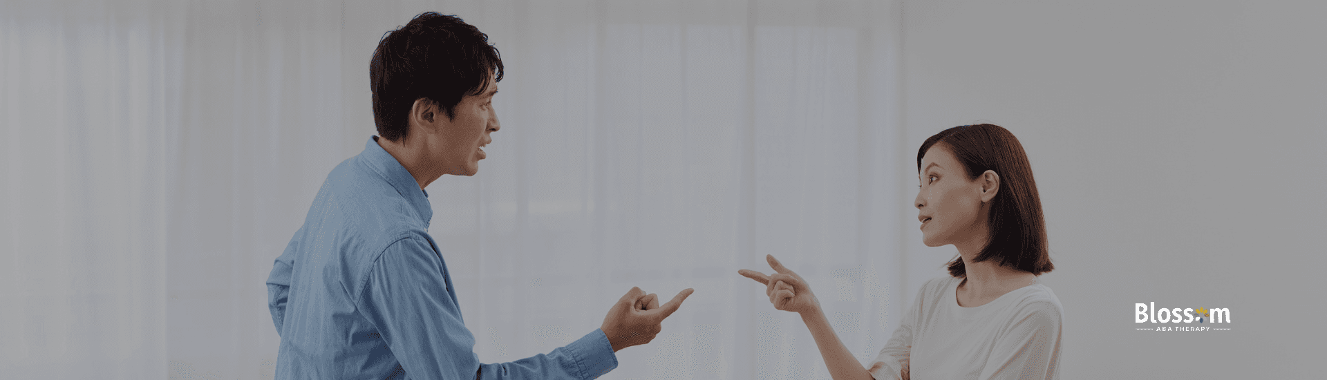 A man and woman in a living room having a heated argument while pointing fingers at each other. The scene is set within a teal and purple border featuring the Blossom ABA Therapy logo and colorful petals.