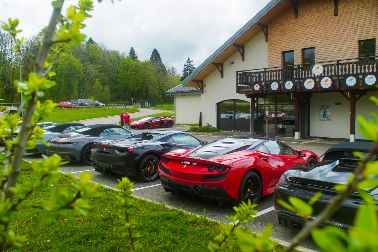 Voitures de sport garées devant un chalet à balcon en bois, dont une rouge au premier plan