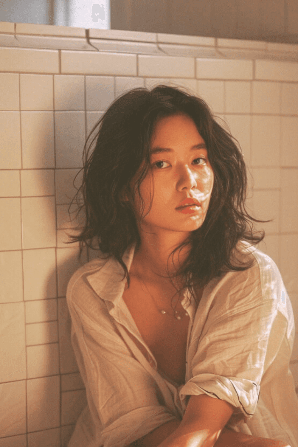 Postpartum mother resting against bathroom tiles, soft light on skin, quiet moment of recovery after childbirth