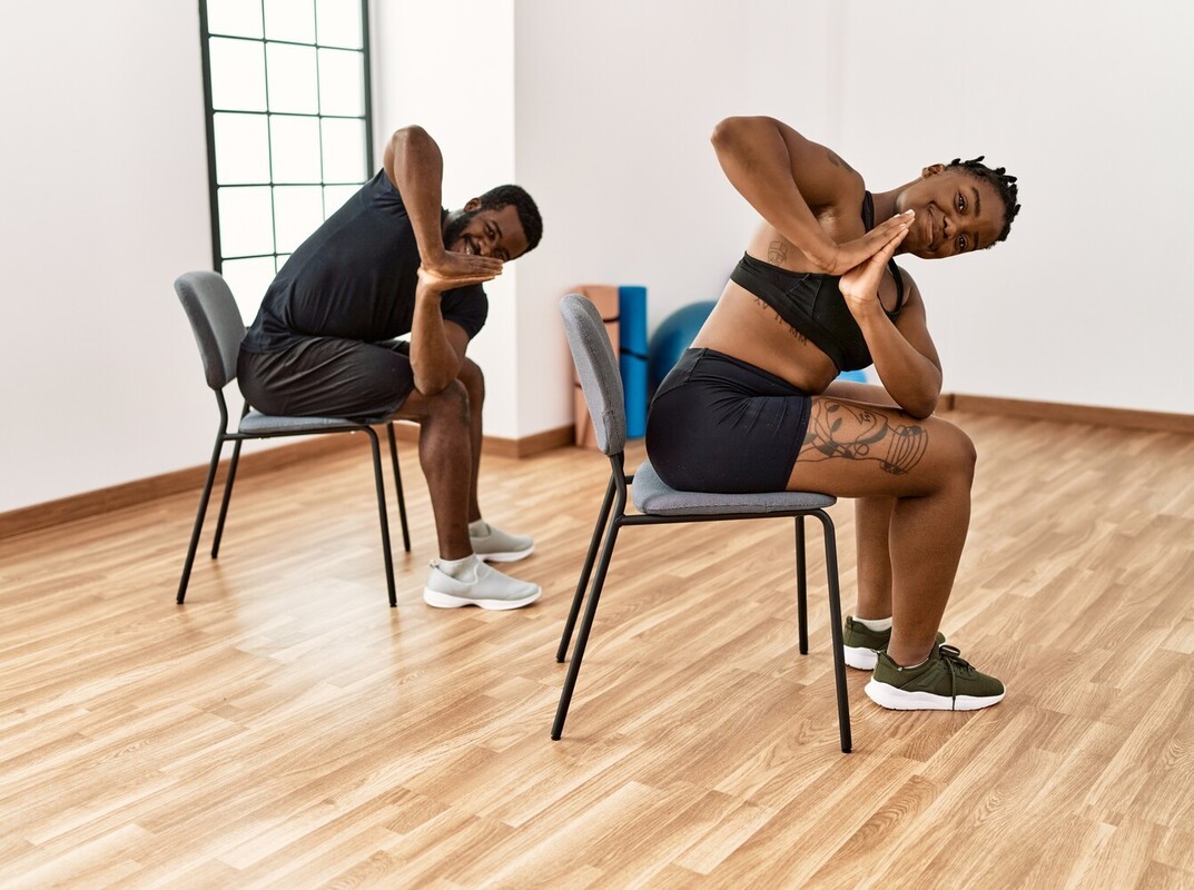 young couple doing seated twist chair exercises for beginners weight loss in a gym studio