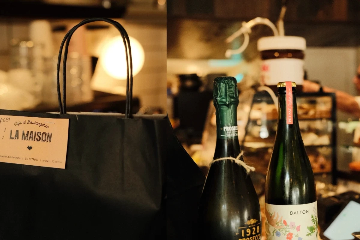 קומפוזיציה המציגה מיתוג ואריזה של בית מאפה. בצד אחד שקית נייר ממותגת של LA MAISON ובצד השני בקבוקי יין ופרוסקו על רקע אווירת בית קפה, מאת Shiriz Photography הצלמת שירי עציץ.