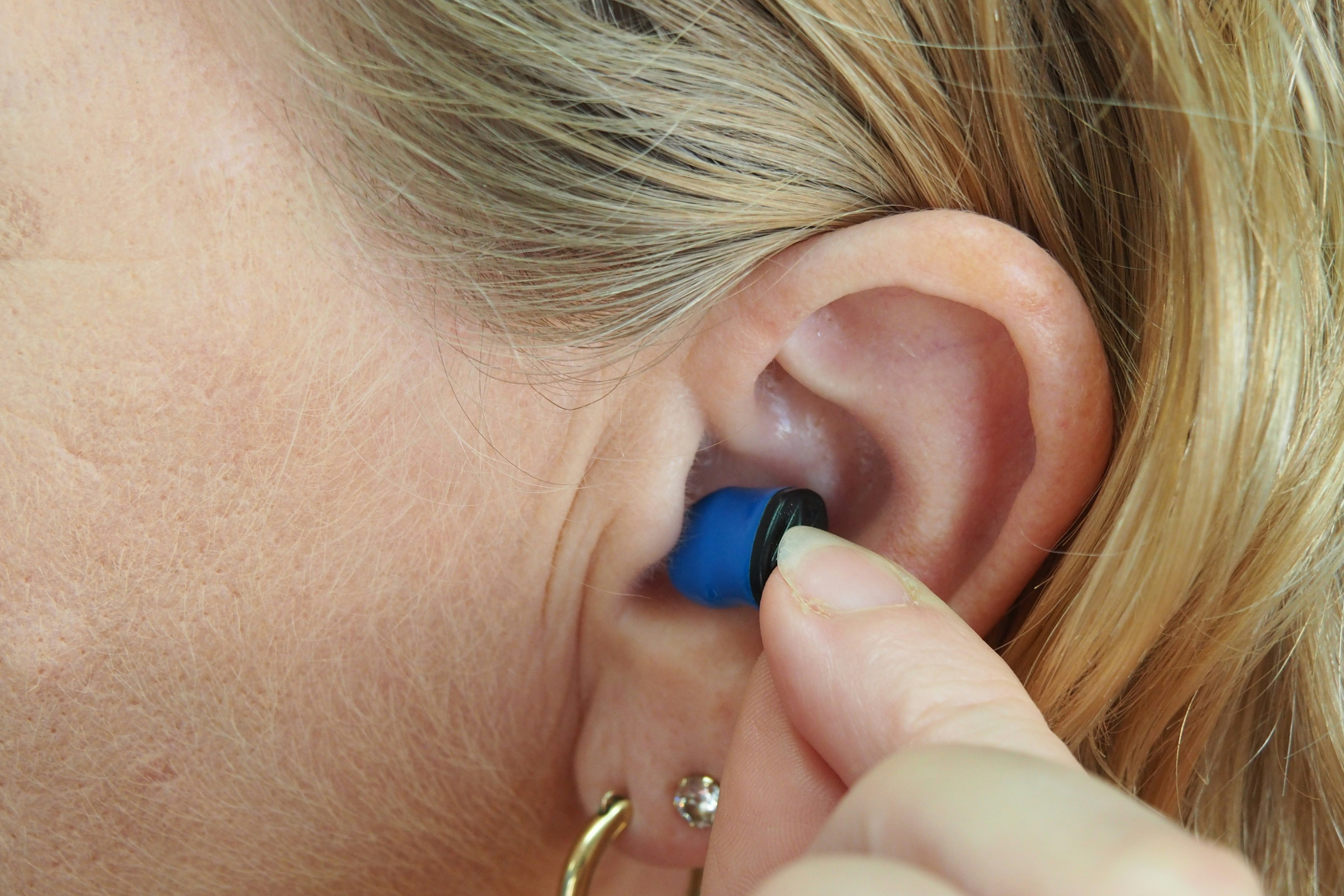 A close-up of a person inserting a small blue hearing aid into their ear.