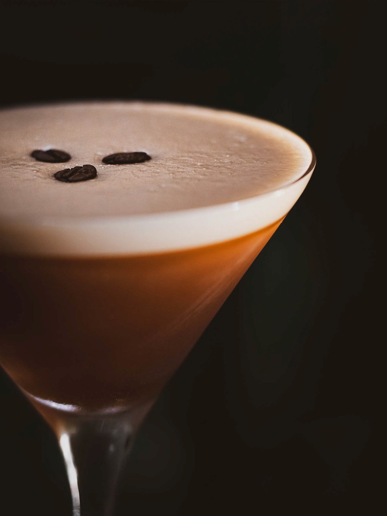 Close-up of a coffee cocktail in a martini glass, garnished with three coffee beans.