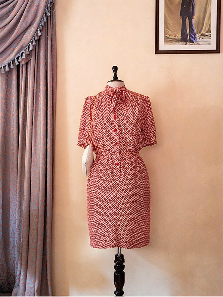 70s vintage Nina Ricci red dress with geometric print, puff sleeves, front buttons, and self-tie neck detail — elegant and easy daywear silhouette.