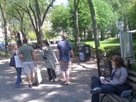 A photo of a group of people carrying bags near a park.