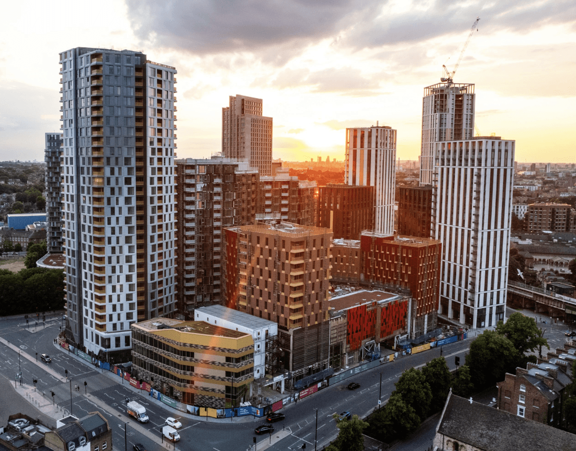 A smiling man with curly hair is sitting at a desk, looking at the camera, with a laptop and a lamp in the background.
