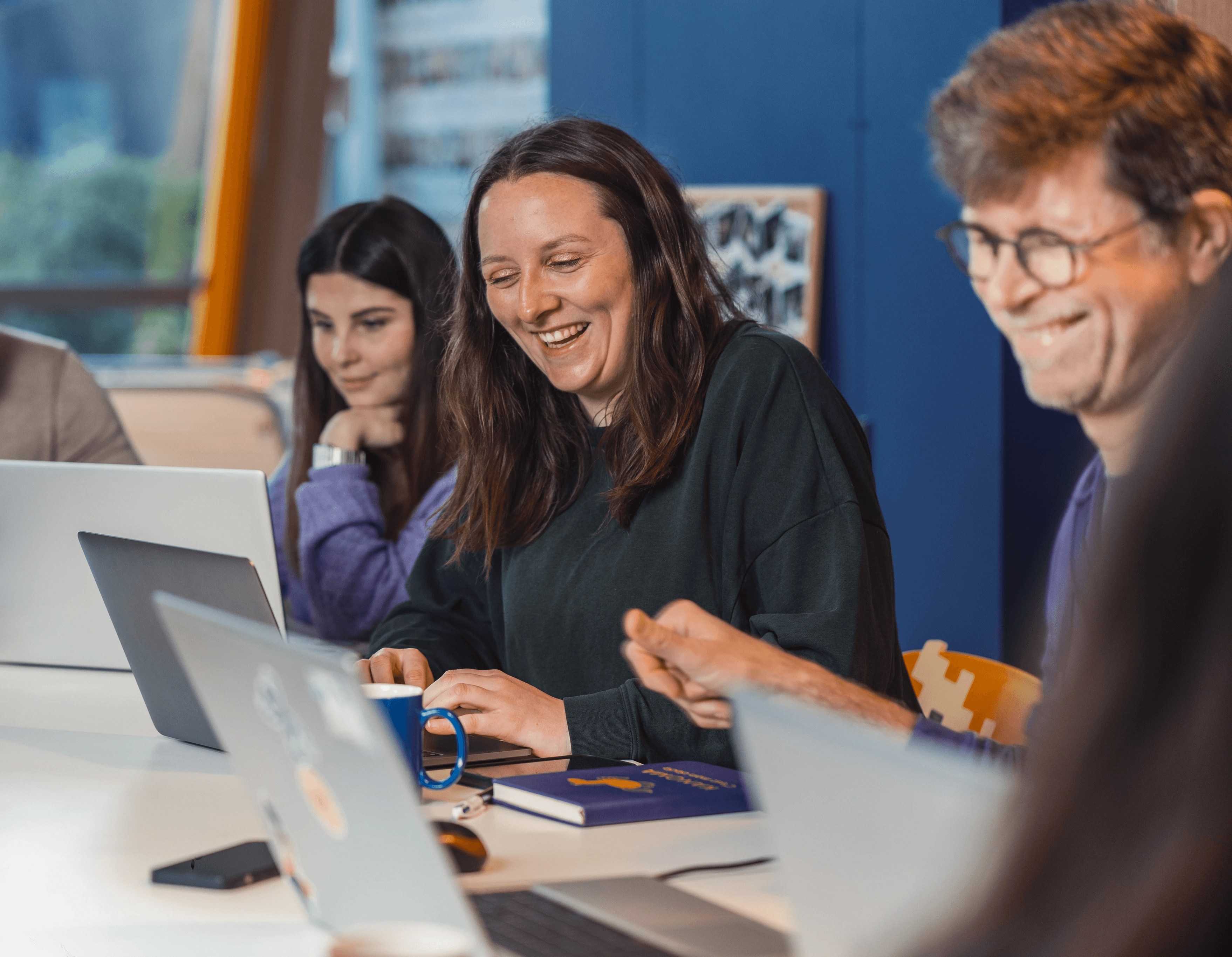 trois personnes qui travaillent sur leur ordinateur, discutent et rigolent