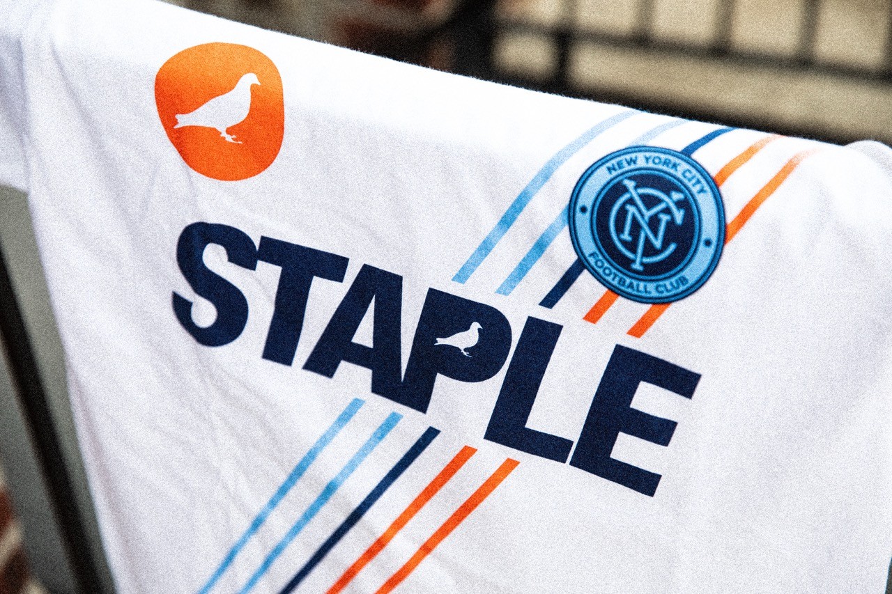 Close-up of Staple x NYCFC graphic on a white shirt featuring the NYCFC crest and diagonal stripe design.