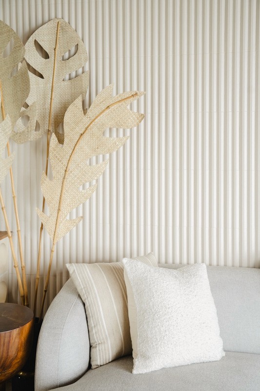 Cozy living room corner with neutral sofa, textured pillows, and woven palm leaf decor against a ribbed cream wall.