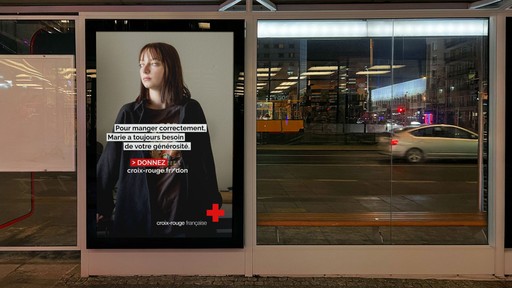 Affiche publicitaire de la Croix-Rouge française dans un abribus la nuit. L'affiche montre le portrait d'une jeune femme et un message d'appel aux dons : "Pour manger correctement, Marie a toujours besoin de votre générosité."