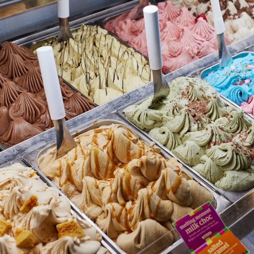 ਮੇਟਲ ਦੀ ਤਰਫਾਂ ਵਿੱਚ ਖੜ੍ਹੇ ਹੋਏ ਸਕੂਪਾਂ ਵਿੱਚ ਚਾਕਲੇਟ, ਕੈਰਮਲ, ਪੁੰਡ ਅਤੇ ਫਲਾਂ ਦੇ ਵੱਖ-ਵੱਖ ਜੇਲਾਟੋ ਸੁਆਦਾਂ ਦੀ ਪ੍ਰਦਰਸ਼ਨੀ।