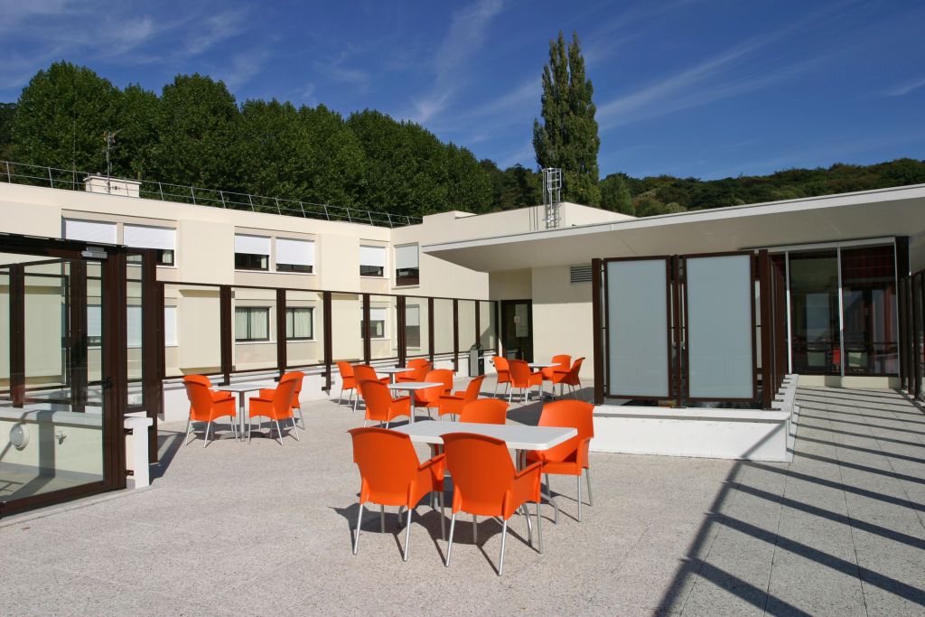 Outdoor patio with bright orange modern chairs, white architectural elements, tree-lined backdrop, and scenic mountain views