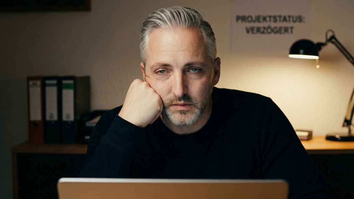 Erschöpfter Mitarbeiter stützt den Kopf am Schreibtisch als Warnsignal für Burnout	