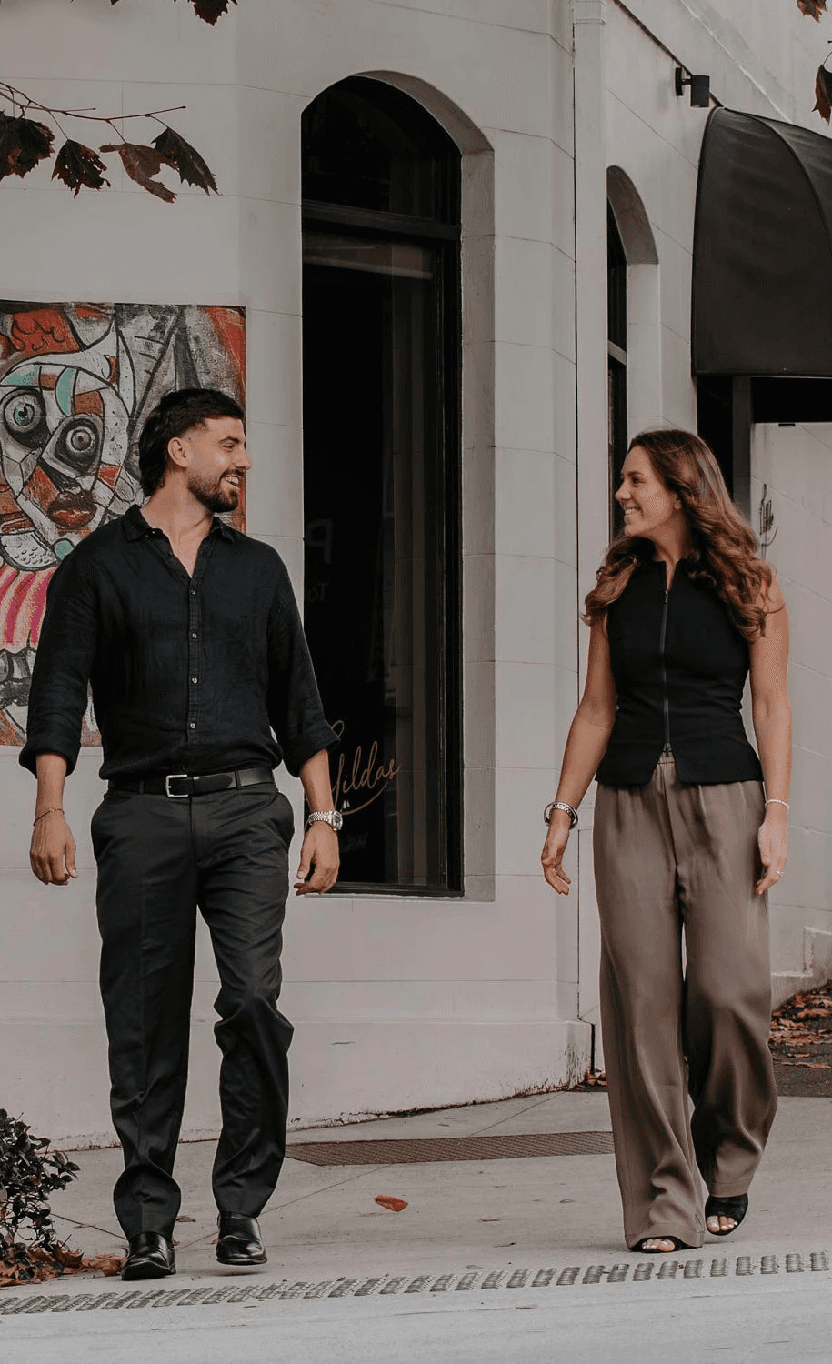 Two smiling people walk together on a city sidewalk.