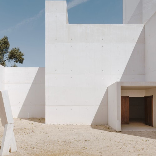 极简主义的白色混凝土建筑，带有几何形状、大型开放入口，沙地前景在湛蓝的天空下。