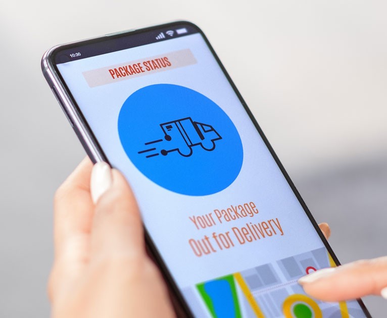 Hands holding a cell phone displaying an image of a mail tracking application.