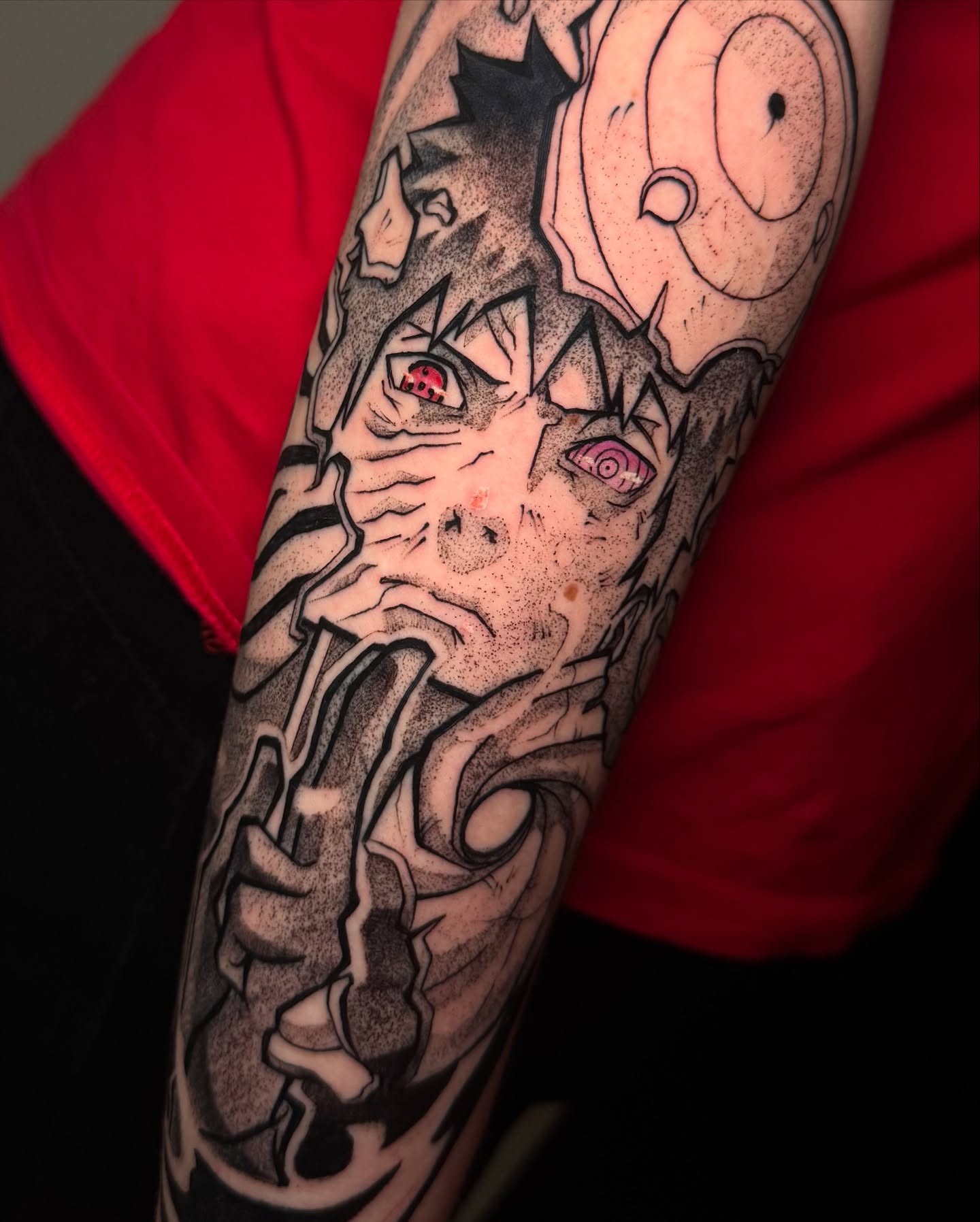 A grayscale anime-style tattoo of a character with spiky hair and a headband, holding a kunai.  The tattoo is on someone's forearm.