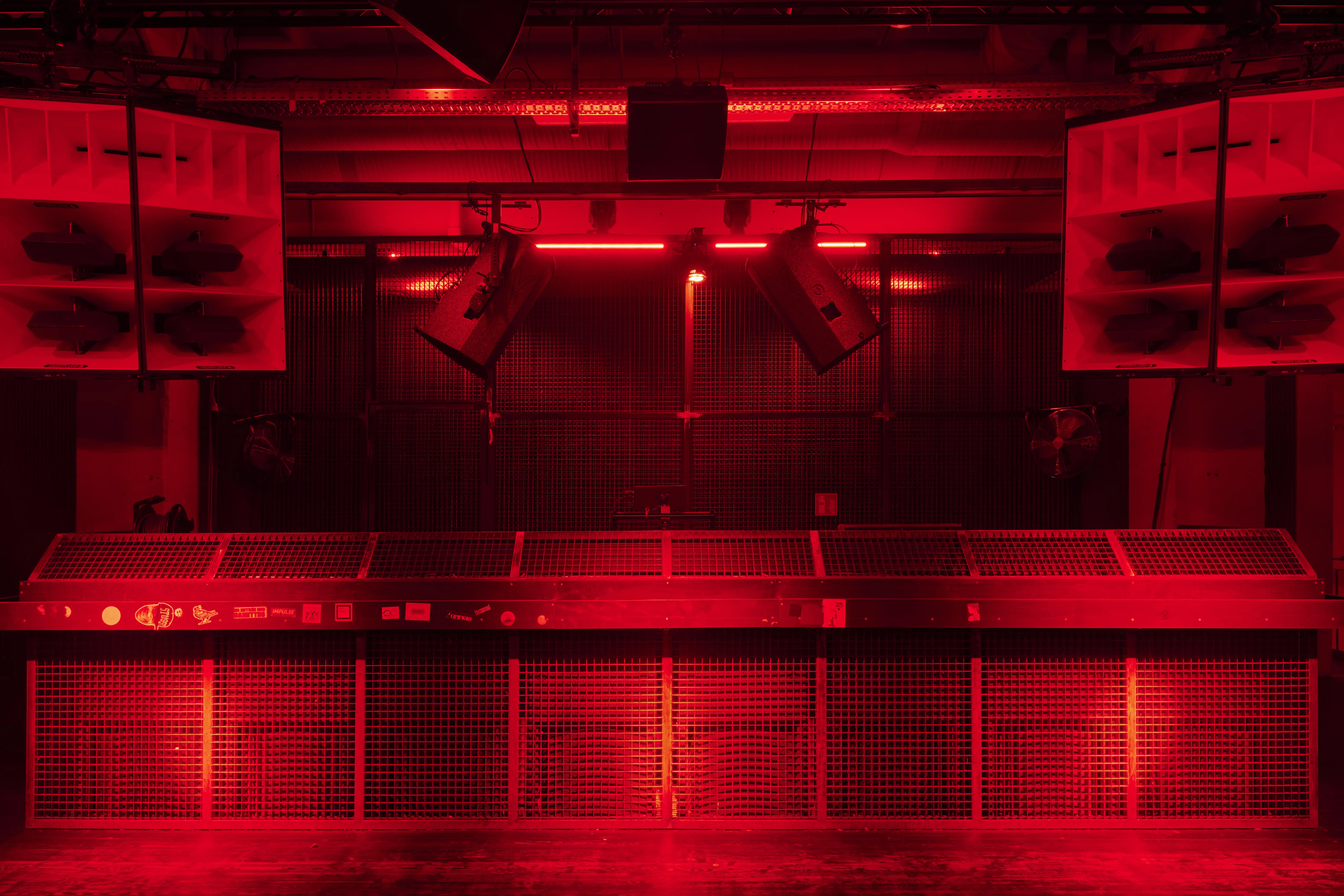 DJ booth at TRESOR GLOBUS in deep red light with a perforated metal front, flanked by white horn speaker arrays and stage spotlights on a black truss wall.