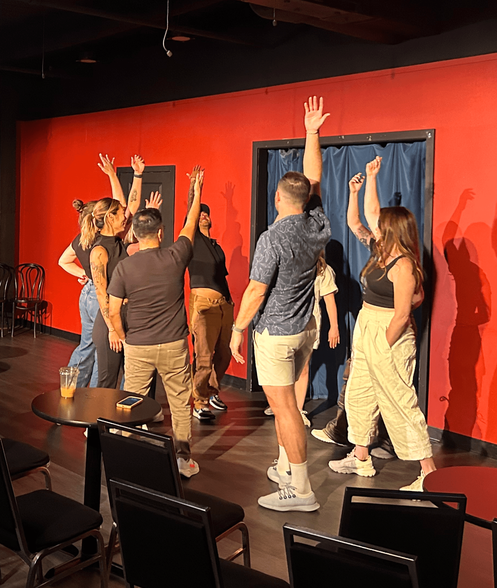 Group of people standing on a small stage with raised hands, participating in an interactive activity in a theater setting.