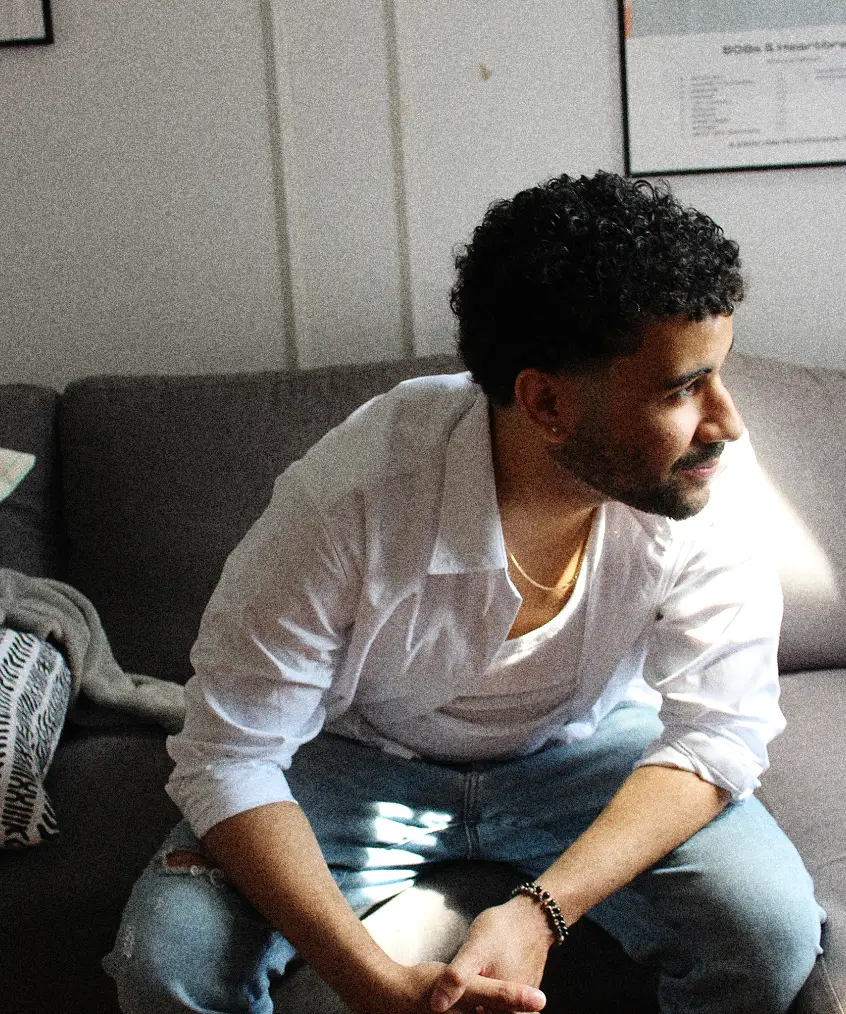 Karim sitting on a sofa in a bright studio space, looking to the side.