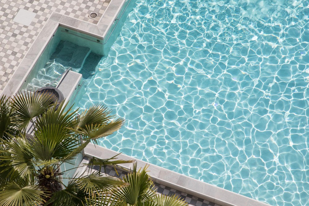Aerial view of a sunlit swimming pool with shimmering water and palm trees along the edge.