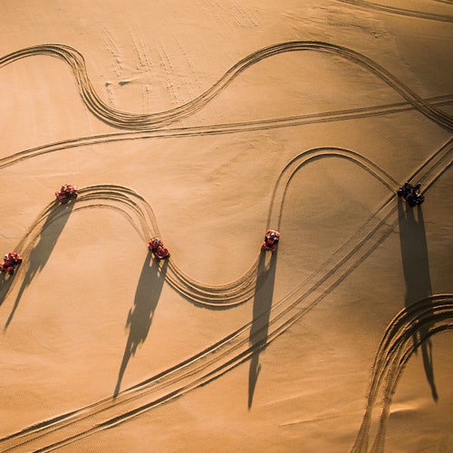 五辆全地形车在沙地上划出弧形轨迹的鸟瞰图,阳光下投射出长长的影子。