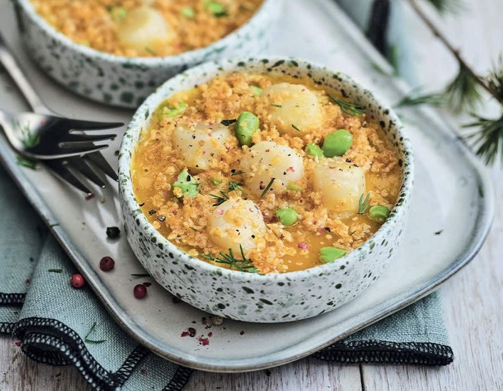 Bol en céramique mouchetée blanc et vert garni de noix de Saint-Jacques, quinoa et fèves, servi sur plateau avec fourchette
