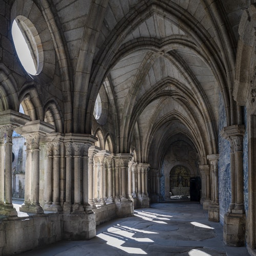Stone cloister with arched ceiling and columns, illuminated by natural light from large windows.