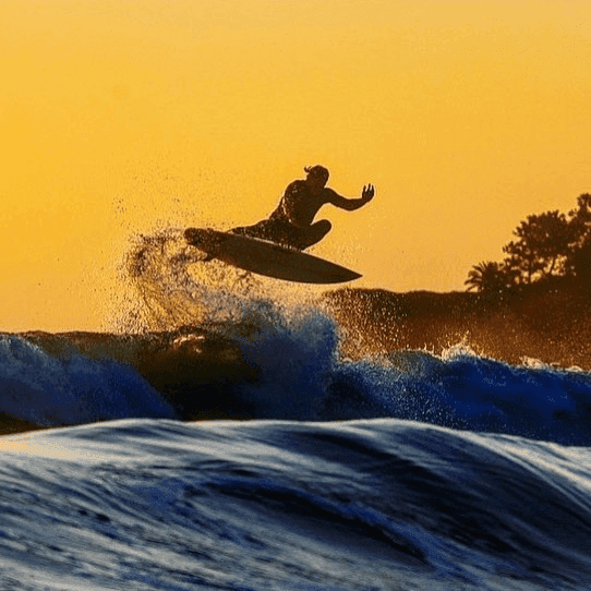 Surfer jumping over a wave at sunset – surfboard rental in dana-point.