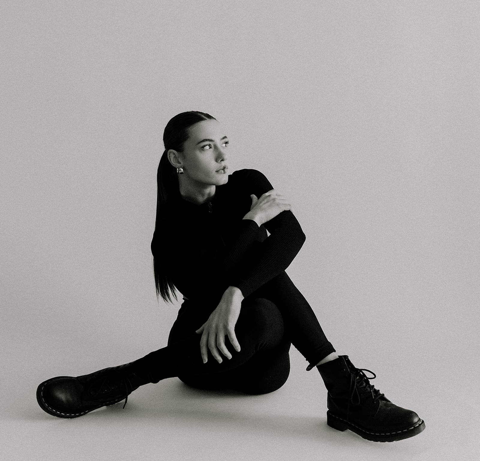 A black-and-white portrait of the model in a seated pose, emphasizing the minimalist and professional environment of Revelator Studio, captured by photographer Justin Posey.