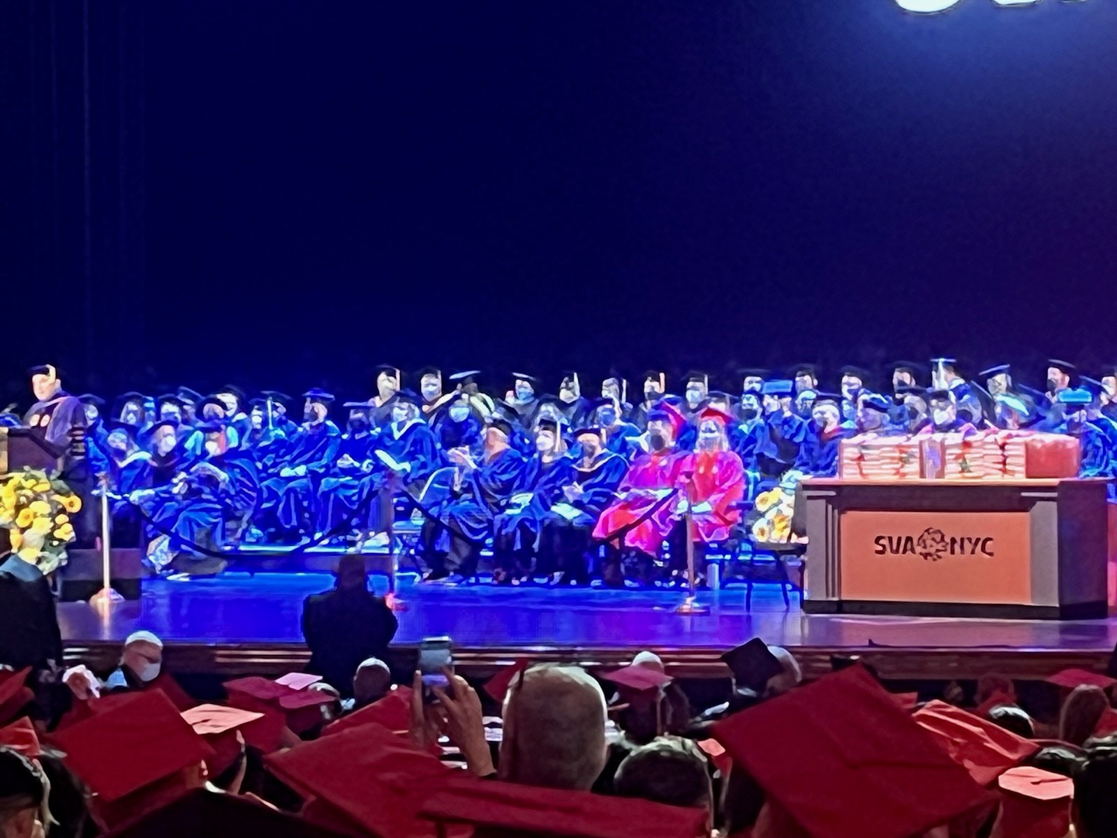 A photo of a group of grad students sitting on a stage, in a festive hall.