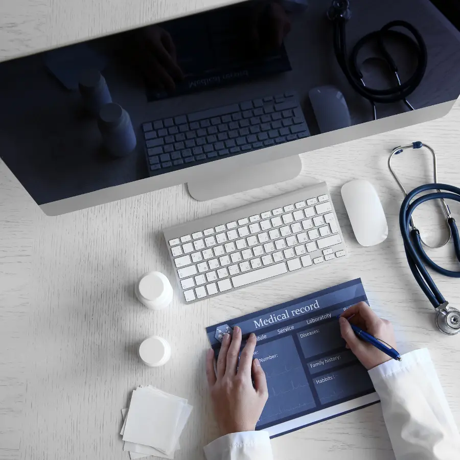 AI solutions for doctors enhancing medical documentation with a physician filling out a medical record alongside a computer and stethoscope