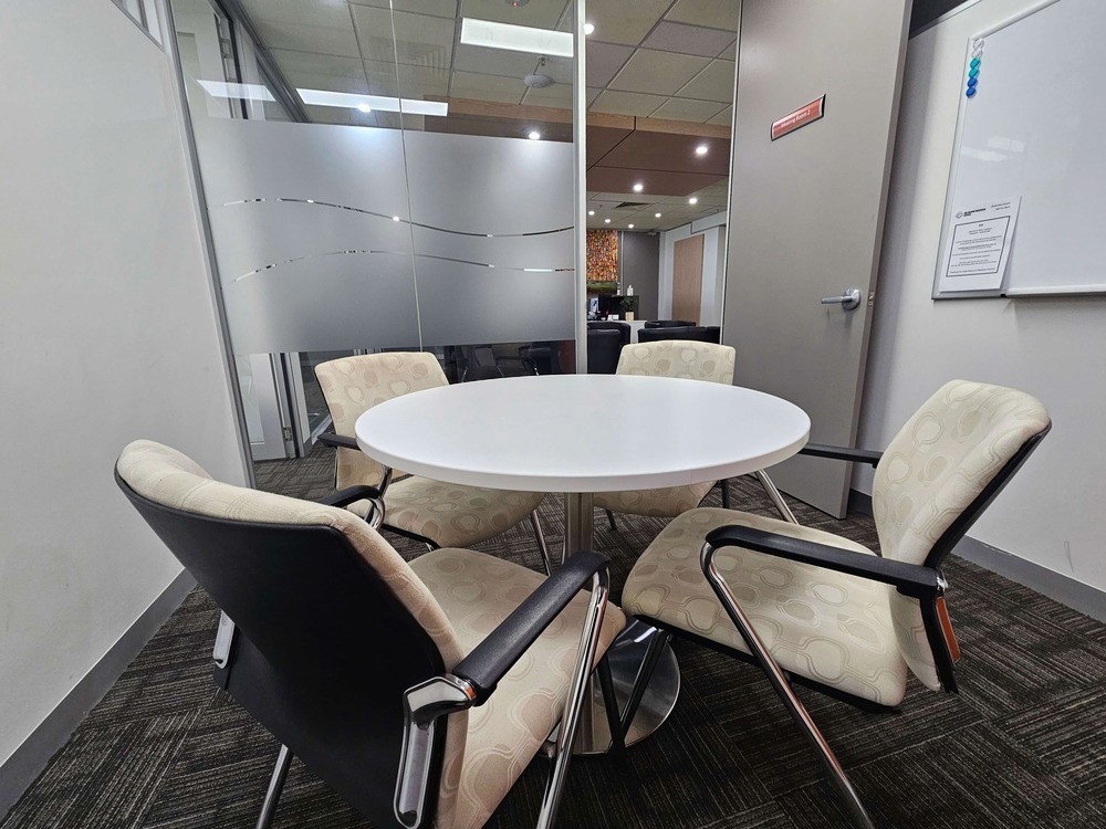 A small and secure room for mediation services, featuring four seats around a small round table and a whiteboard on the wall.