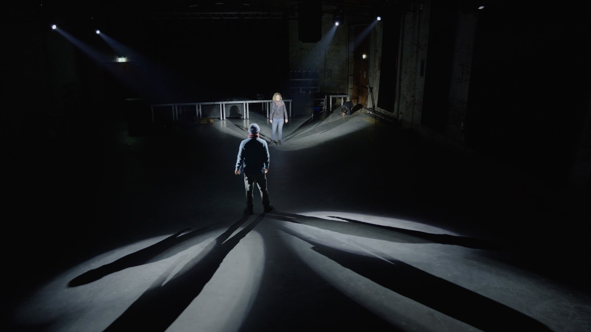 Two people on a dark stage, lit by spotlights.