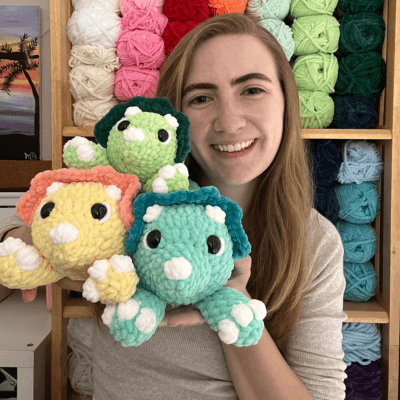 A person with long hair smiles joyfully against a vibrant orange background, wearing a knit mustard-yellow sweater, exuding warmth and happiness.