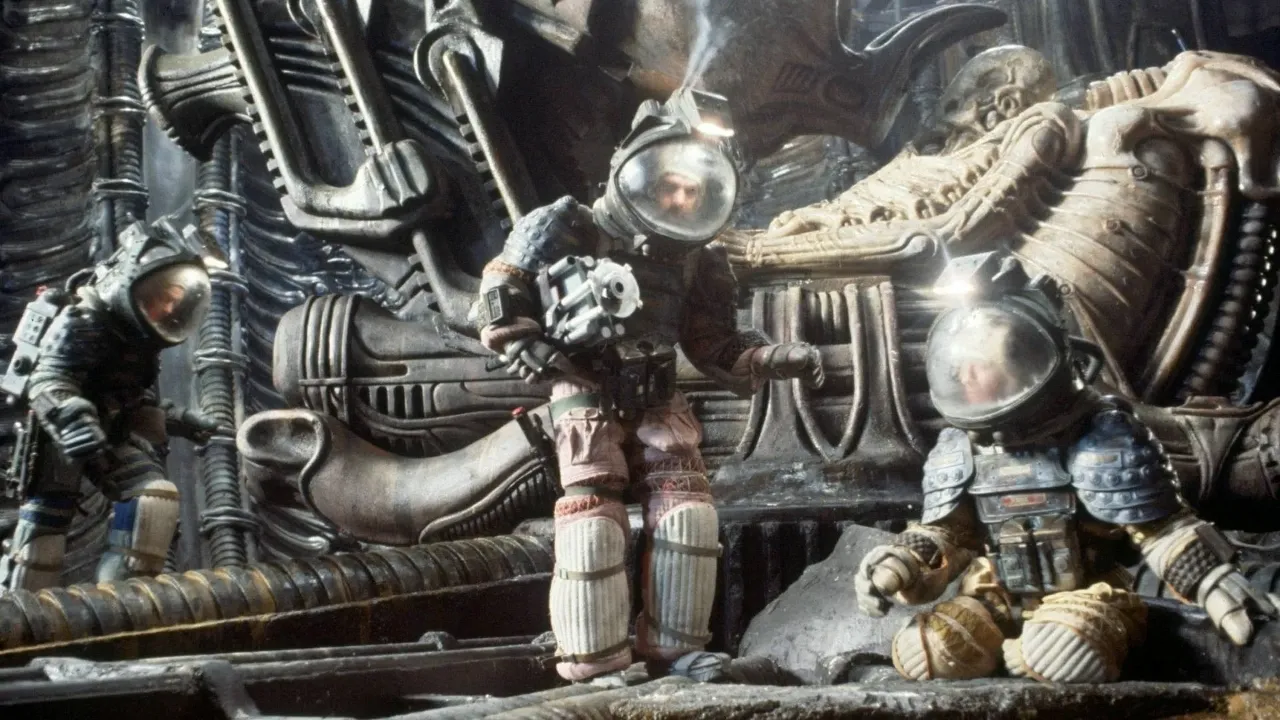 Three astronauts in detailed, bulky space suits explore an intricately designed, alien spacecraft environment featuring elaborate machinery and structures.