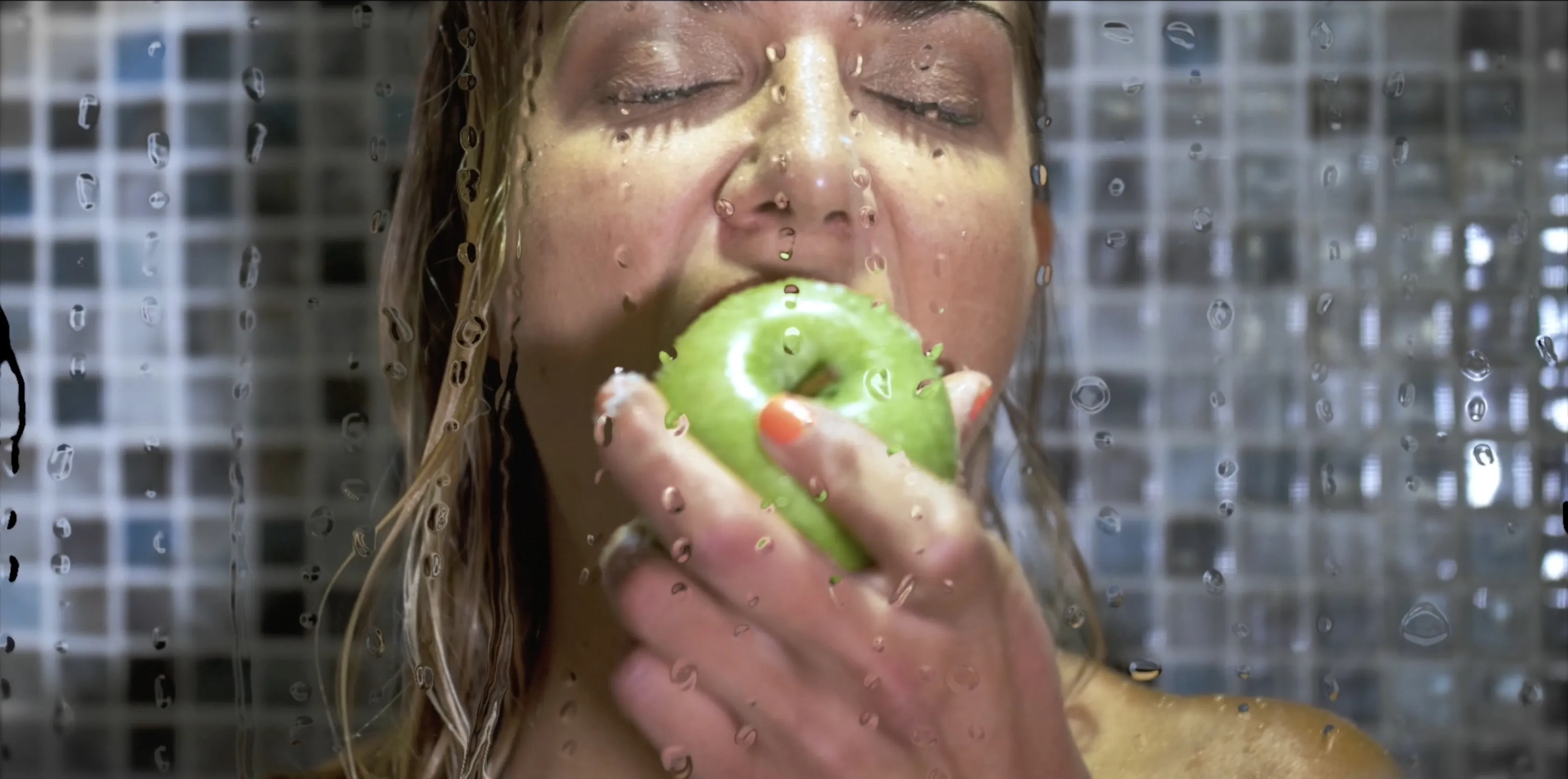 A person enjoying a green apple in a steamy shower with water droplets on the glass and a mosaic tile background, creating a refreshing and serene atmosphere.