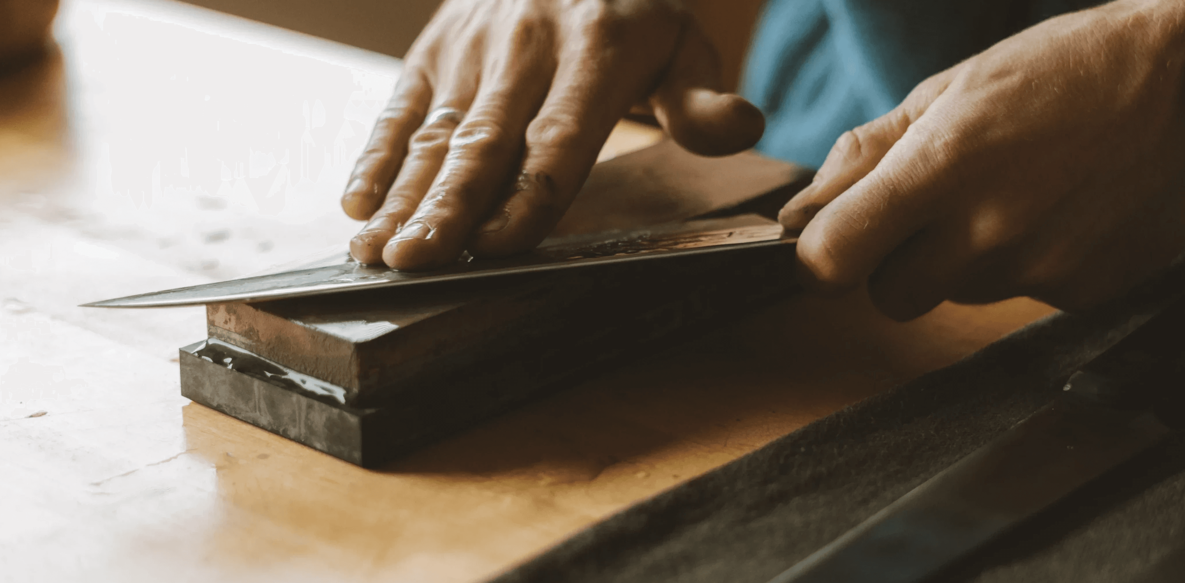 A hand carefully stropping a Damascus steel knife on a leather surface to achieve a polished, razor-sharp edge.