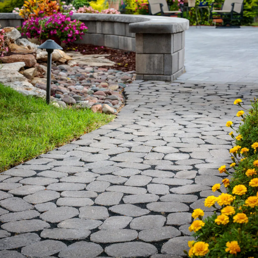 Textured gray paver walkway passing between flowers, lawn and garden stonework.