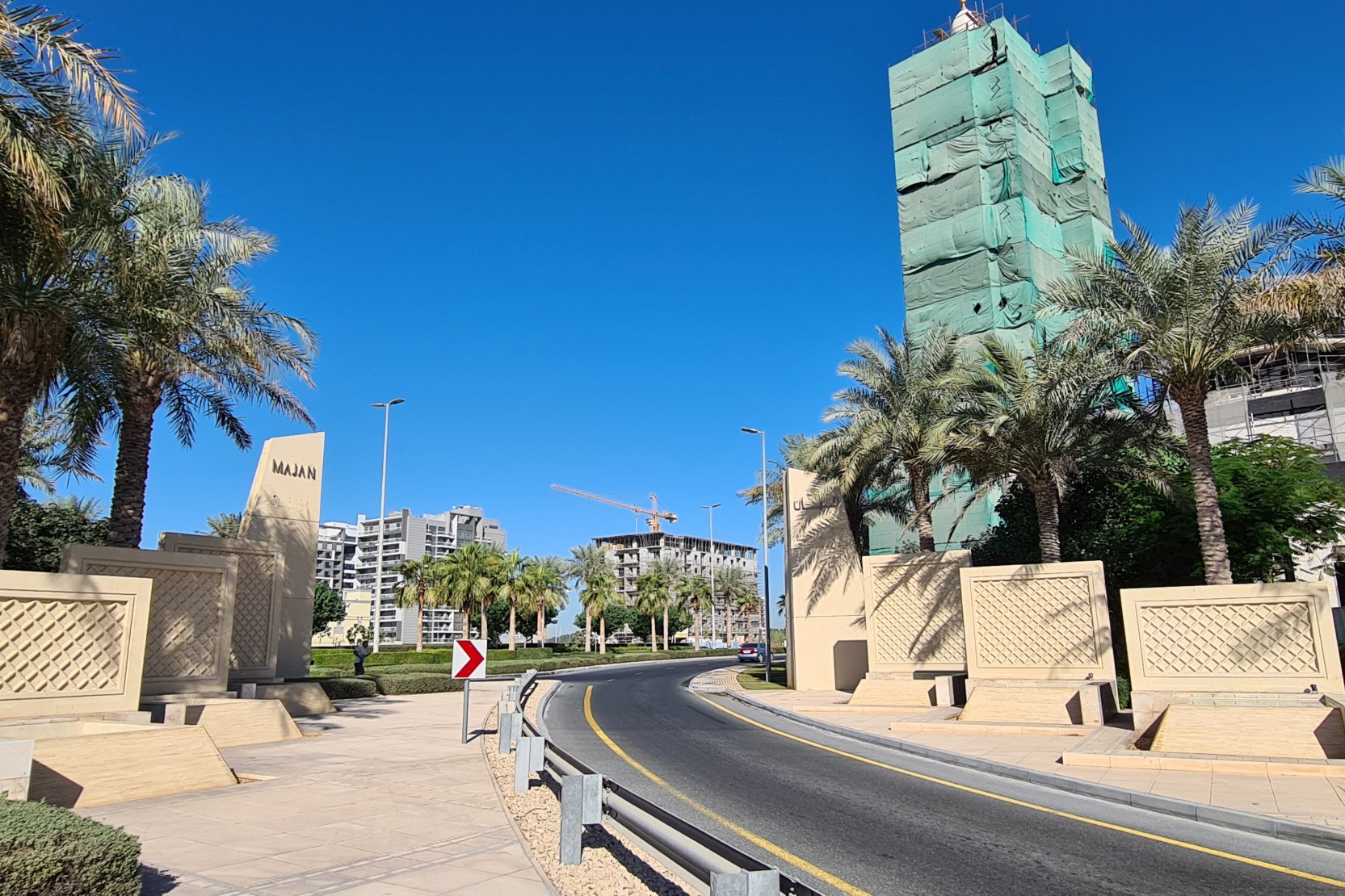 The entrance to the Majan community in the UAE, showcasing palm trees, decorative stone walls, and new developments.