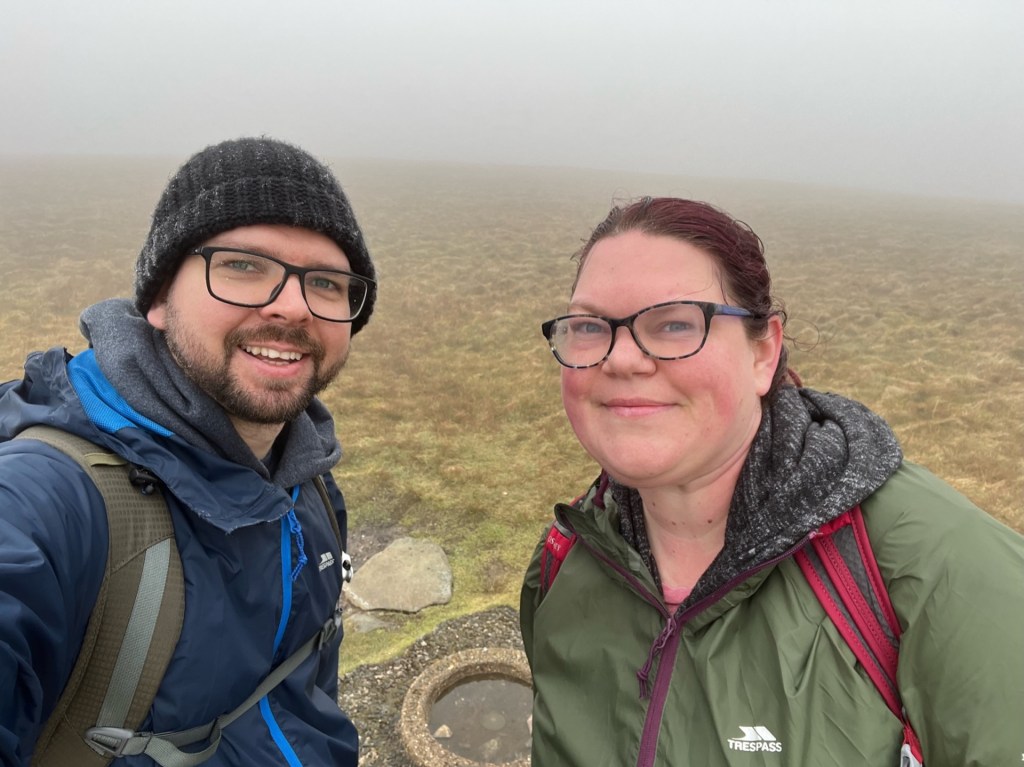 A selfie of Martin and April either side of Branstree Fell summit cairn. Thick fog in the background hides any kind of view.