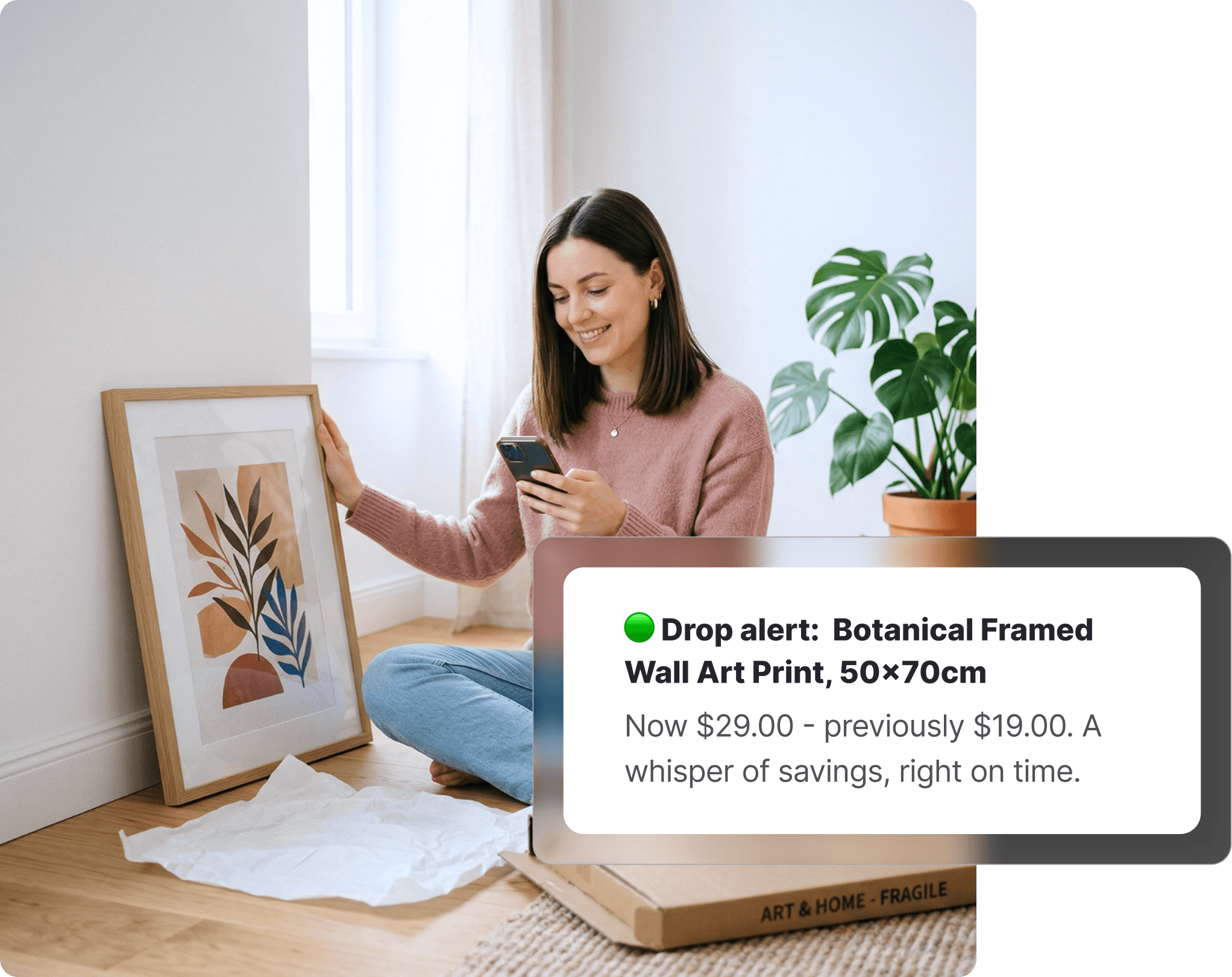 Woman sitting on the floor checking her phone next to an unboxed Kmart-style framed botanical art print, with a monstera plant and a fragile delivery box visible beside her.