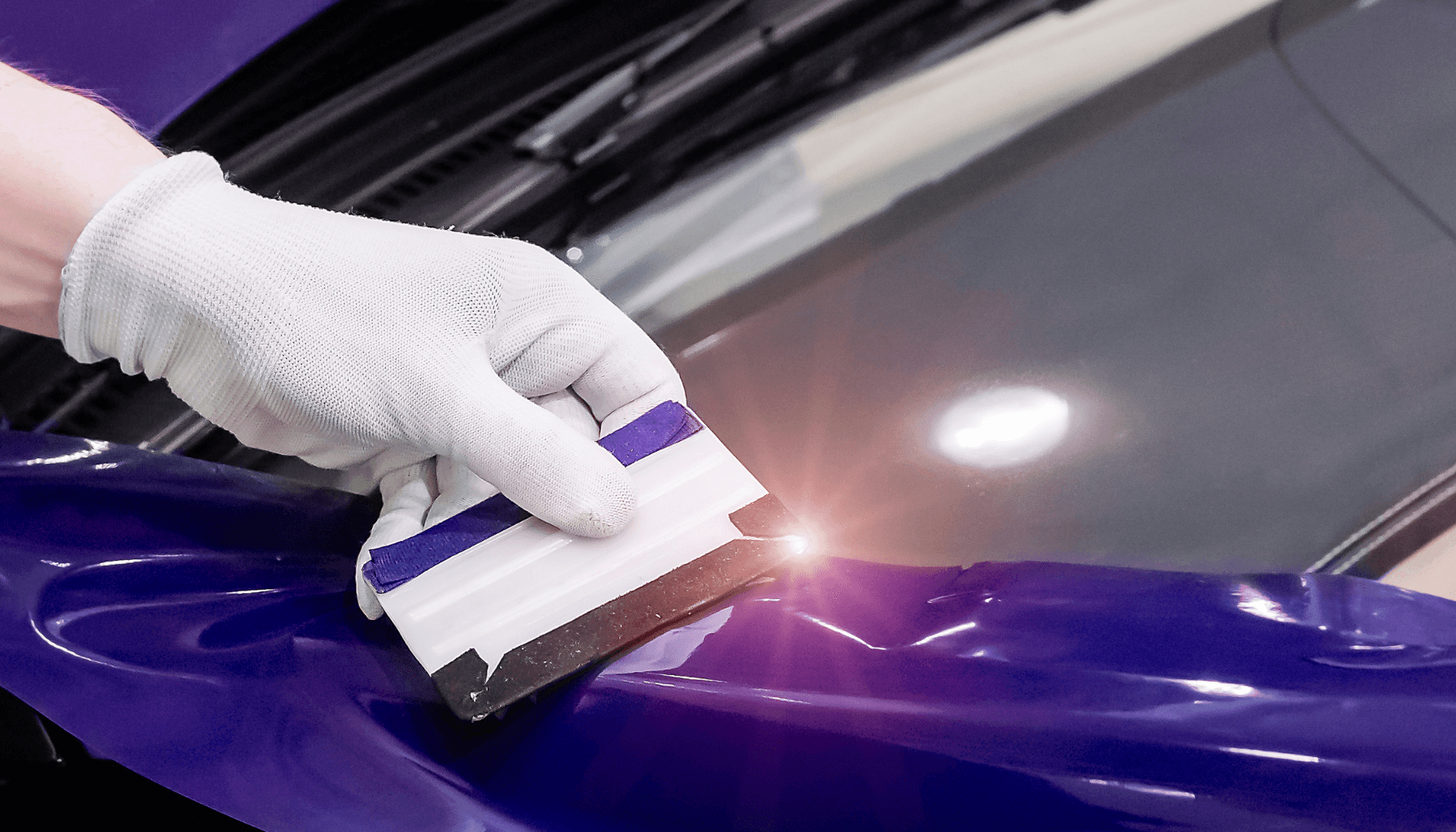 Hand mit Handschuh bringt blaue Folie beim Car Wrapping mit einer Rakel auf ein Auto auf.
