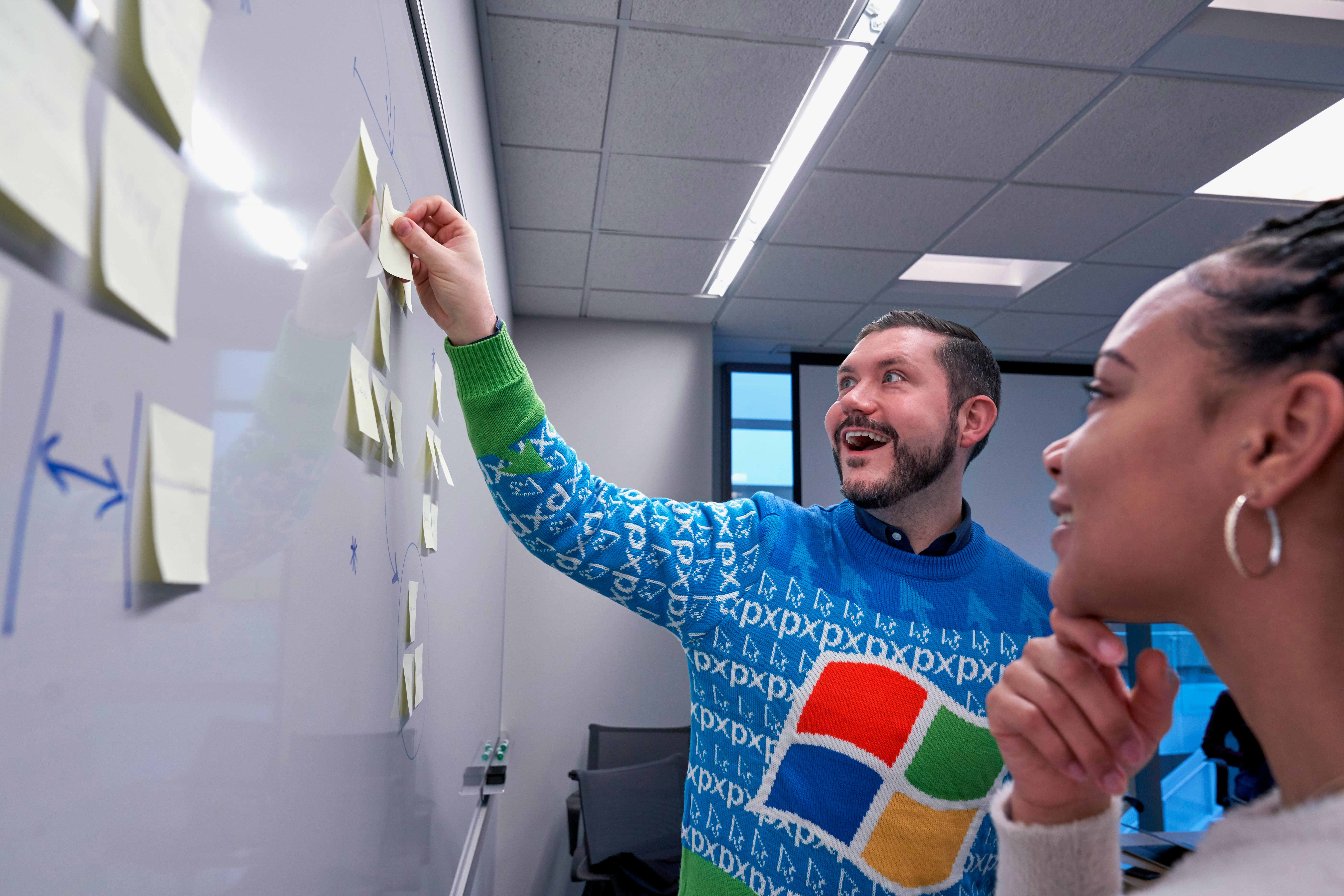 Man wearing blue Windows sweater holding sticky note on white board