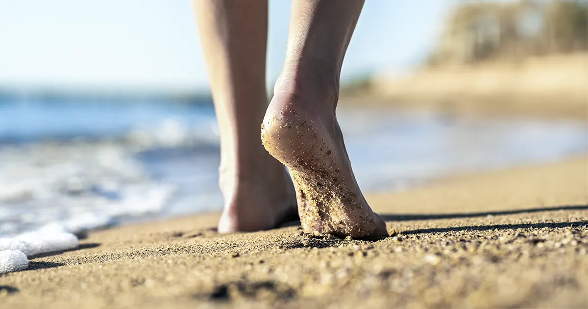 Bilde av to føtter som vandrer langs en strand.