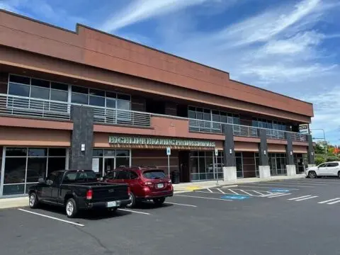 A two-story commercial building with a brown roof and parked cars in front, under a clear blue sky.