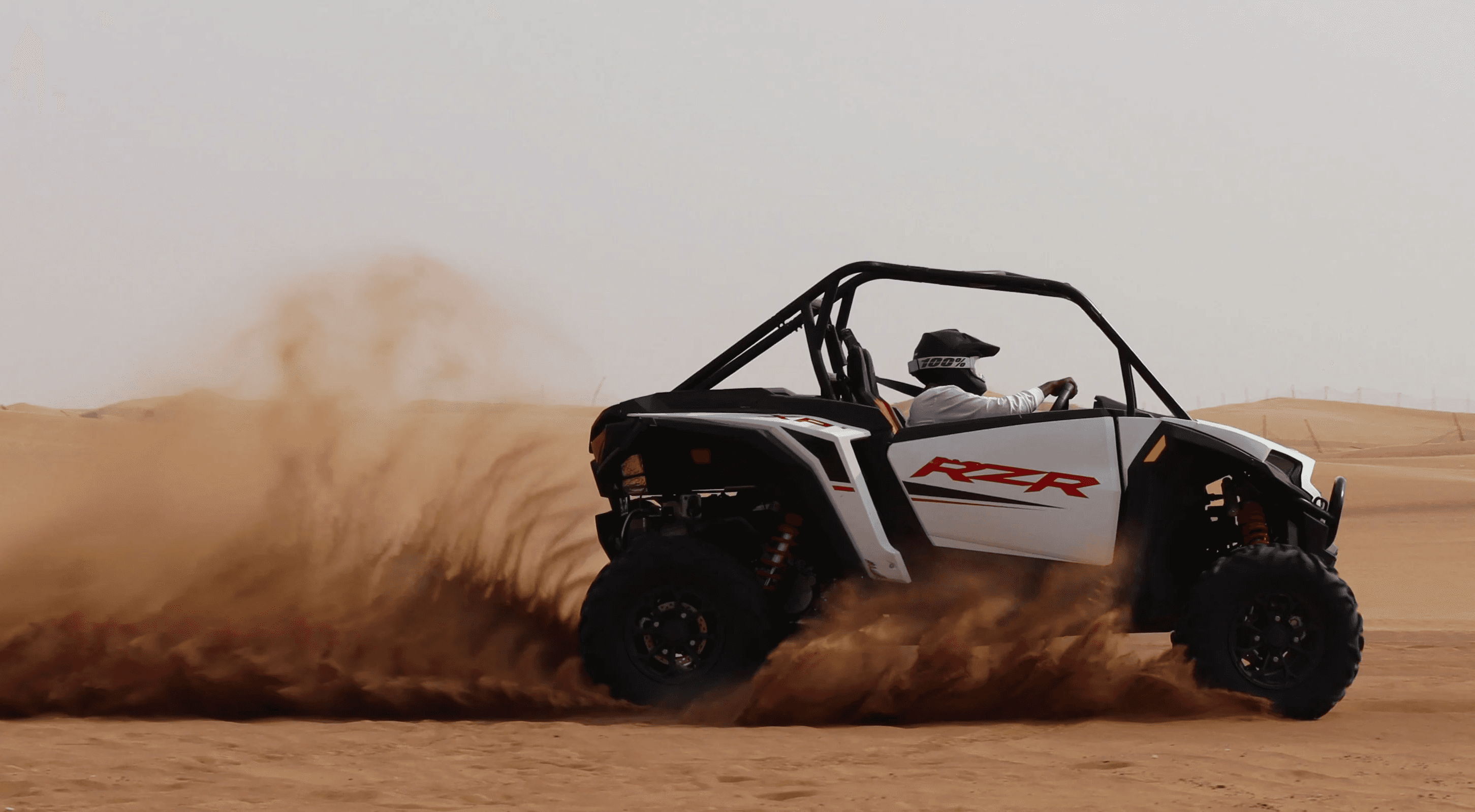 A white Polaris RZR 1000cc XP 2-seater buggy drifting through the high red dunes of Lehbab, Dubai, kicking up sand during an off-road desert adventure